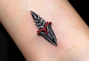A hand-carved flint arrowhead in gray with red cord wrapping, symbolizing strength and survival tattoo idea