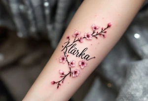 Klárka in delicate script, surrounded by cherry blossom petals in soft pink. tattoo idea