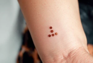 Three copper-toned dots forming an inverted triangle near the base of the thumb, signifying feminine energy and creativity. tattoo idea
