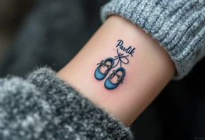 Pavlík written above a tiny pair of baby shoes in dusty blue. tattoo idea
