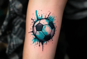 A small behind-the-ear soccer ball tattoo in black with a splash of teal paint. tattoo idea