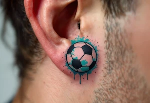 A small behind-the-ear soccer ball tattoo in black with a splash of teal paint. tattoo idea