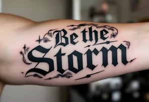 "Be the Storm" in sharp serif font, black ink with storm cloud shading and lightning bolt details in gray. tattoo idea