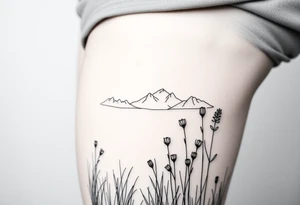 A field with long grass and flowers with mountains in the background tattoo idea