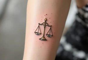 A delicate Libra constellation in shimmering gold ink wraps around a pair of balanced silver scales. tattoo idea