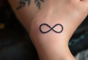 A lace-textured infinity outline in dark gray, with a soft burgundy heart sewn into the design. tattoo idea