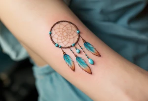 Dreamcatcher (česky lapač snů) tattoo featuring soft turquoise and beige feathers, a brown woven hoop with light blue beads, symbolizing protection and peaceful dreams in a delicate, boho style. tattoo idea