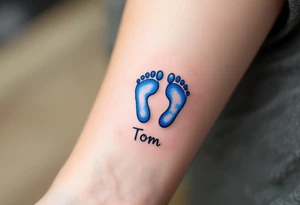 A pair of tiny blue footprints with the son's name Tom in elegant black script beneath. tattoo idea