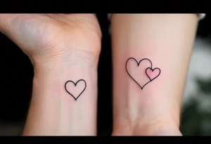A pair of connected black line-drawn hearts, the first outlined in bold black on wrist and the second filled with soft pastel pink on wrist. tattoo idea