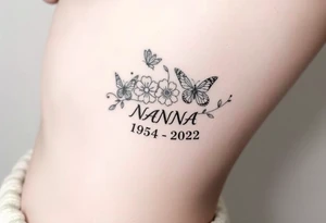 flowers and butterflies with the name “NANA” and the date “1954-2022” mixed all together on the side of the rib cage tattoo idea