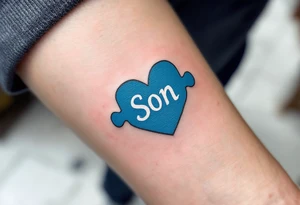 A puzzle piece in bright blue labeled “Son,” fitted perfectly into a black outline of a heart. tattoo idea