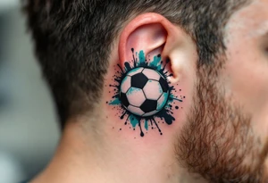 A small behind-the-ear soccer ball tattoo in black with a splash of teal paint. tattoo idea