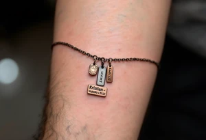 A dainty chain bracelet tattoo with hanging charm tags engraved with "Kristian – 15.8.2018 v 21:21" in metallic bronze ink tattoo idea
