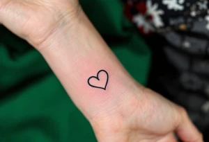 A pair of connected black line-drawn hearts, the first outlined in bold black on wrist and the second filled with soft pastel pink on wrist. tattoo idea