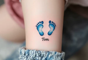A pair of tiny blue footprints with the son's name Tom in elegant black script beneath. tattoo idea