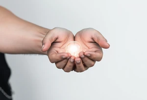 Two hands carefully holding a glowing orb of light, soft realistic shading, warm light radiating from the orb, black and gray tattoo style.” tattoo idea