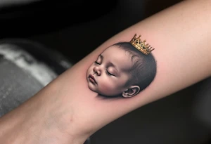 Profile portrait of a baby girl’s sleeping face with a tiny gold crown, shaded in grayscale with realistic detail. tattoo idea