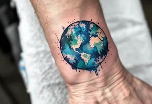 A linework planet Earth filled with watercolor splashes of turquoise, jade, and indigo rests on the inner wrist. tattoo idea