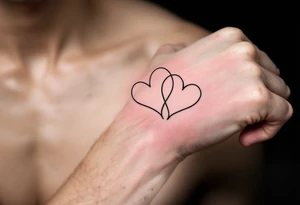 A pair of connected black line-drawn hearts, the first outlined in bold black on wrist and the second filled with soft pastel pink on wrist. tattoo idea