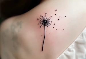 Hand-poked effect dandelion in faded black, looking softly aged, seeds scattered lightly across the shoulder. tattoo idea