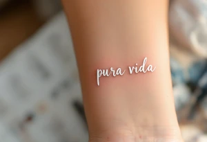 “Pura Vida” in white ink across a tan skin tone, with subtle shadowing for a sun-kissed effect. tattoo idea