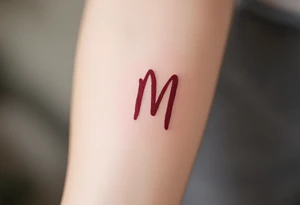 A brush-style "M" in burgundy red, looking bold and spontaneous. tattoo idea