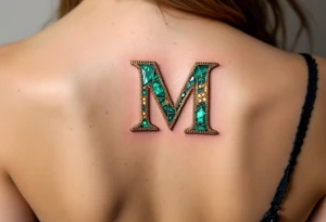 A mosaic-style "M" made of gold and emerald tiles, creating a royal effect. tattoo idea