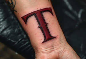 A stitched "T" in burgundy red, designed like embroidery on skin. tattoo idea