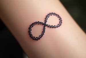 A lace-textured infinity outline in dark gray, with a soft burgundy heart sewn into the design. tattoo idea
