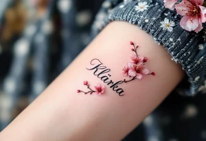 Klárka in delicate script, surrounded by cherry blossom petals in soft pink. tattoo idea