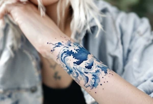 A soft blue watercolor wave wraps around the wrist, fading into foamy white tips. tattoo idea
