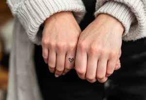 Thin black line tattoos of two hands making a pinky promise, with a tiny red heart between them.
Placement: Side of the index finger or wrist. tattoo idea
