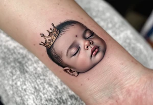 Profile portrait of a baby girl’s sleeping face with a tiny gold crown, with realistic detail. tattoo idea