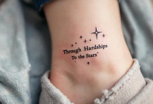 A simple black-ink tattoo wraps “Through Hardships To the Stars” around the ankle, with each word nestled between tiny violet stars. S tattoo idea