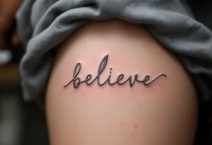 A delicate "Believe" in silver, intertwined with tiny feathers in soft white, symbolizing freedom and trust in the journey. tattoo idea