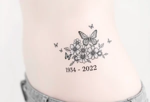 flowers and butterflies with the name “NANA” and the date “1954-2022” mixed all together on the side of the rib cage tattoo idea