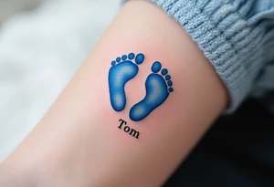 A pair of tiny blue footprints with the son's name Tom in elegant black script beneath. tattoo idea