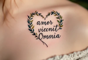 "Amor Vincit Omnia" (Love conquers all) in soft cursive lettering, placed inside a delicate heart made of olive branches, inked in charcoal black with touches of olive green. tattoo idea