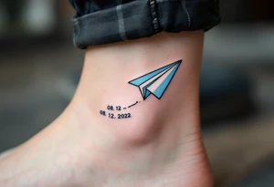 A cartoon-style paper airplane in soft grey and baby blue, trailing a banner with the birthdate 08. 12. 2022. tattoo idea