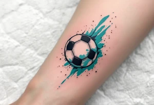 A small behind-the-ear soccer ball tattoo in black with a splash of teal paint. tattoo idea