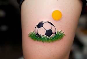 A detailed soccer ball resting on green grass with a bright yellow sun overhead. tattoo idea