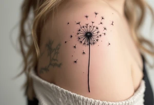 Hand-poked effect dandelion in faded black, looking softly aged, seeds scattered lightly across the shoulder. tattoo idea