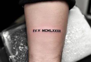 Minimalist IV.V.MCMLXXX tattooed in fine-line black ink on the inner forearm for a birthdate tribute. tattoo idea
