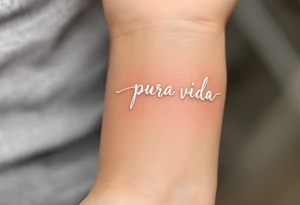 “Pura Vida” in white ink across a tan skin tone, with subtle shadowing for a sun-kissed effect. tattoo idea