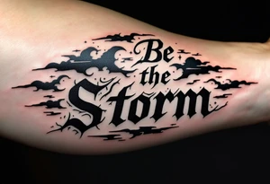 "Be the Storm" in sharp serif font, black ink with storm cloud shading and lightning bolt details in gray. tattoo idea
