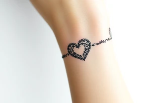 A heart-shaped lace pattern bracelet in black and silver, with a delicate filigree border tattoo idea