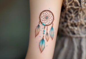 Dreamcatcher (česky lapač snů) tattoo featuring soft turquoise and beige feathers, a brown woven hoop with light blue beads, symbolizing protection and peaceful dreams in a delicate, boho style. tattoo idea