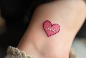 A heart shaded in pinky with Sára in a handwritten-style font inside. tattoo idea
