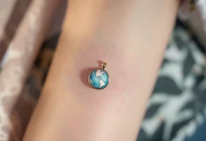 A tiny Earth in subtle sky blue and seafoam green is encased in a thin gold ring like a pendant. tattoo idea