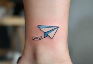 A cartoon-style paper airplane in soft grey and baby blue, trailing a banner with the birthdate 08. 12. 2022. tattoo idea